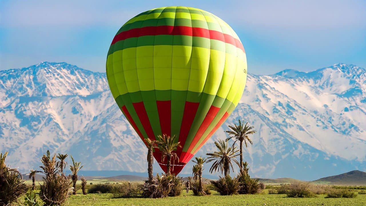 A balloon on the ground with the snow-capped High Atlas and date palms behind it