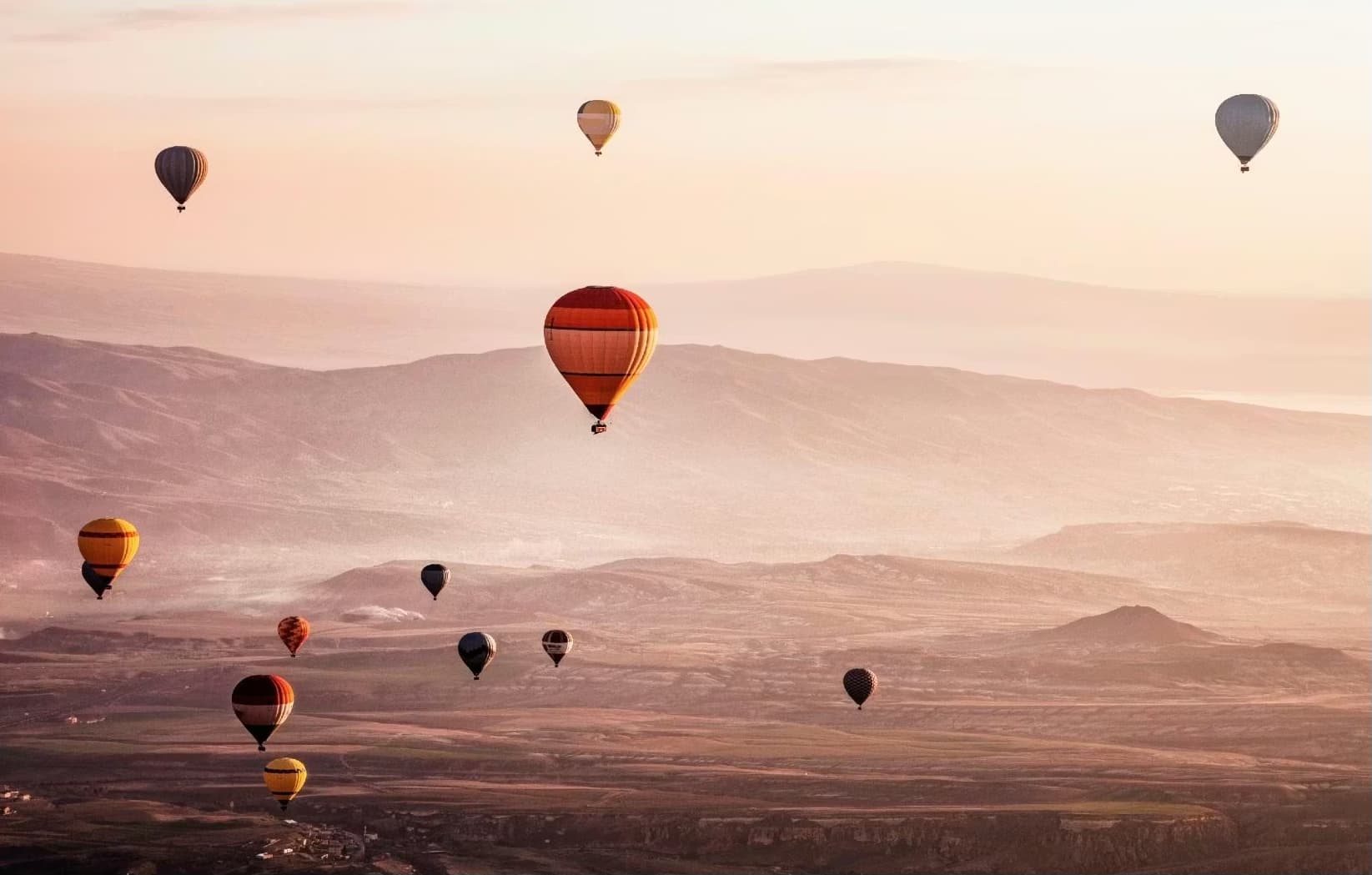 A dozen balloons spread across a hazy valley at first light