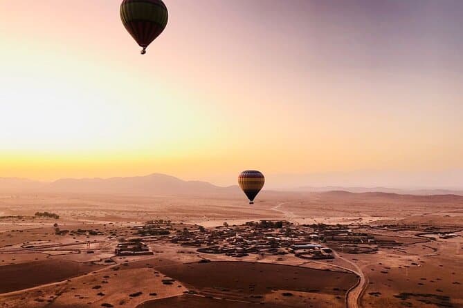 Two balloons over a village on the plain at sunrise, hills in the haze behind