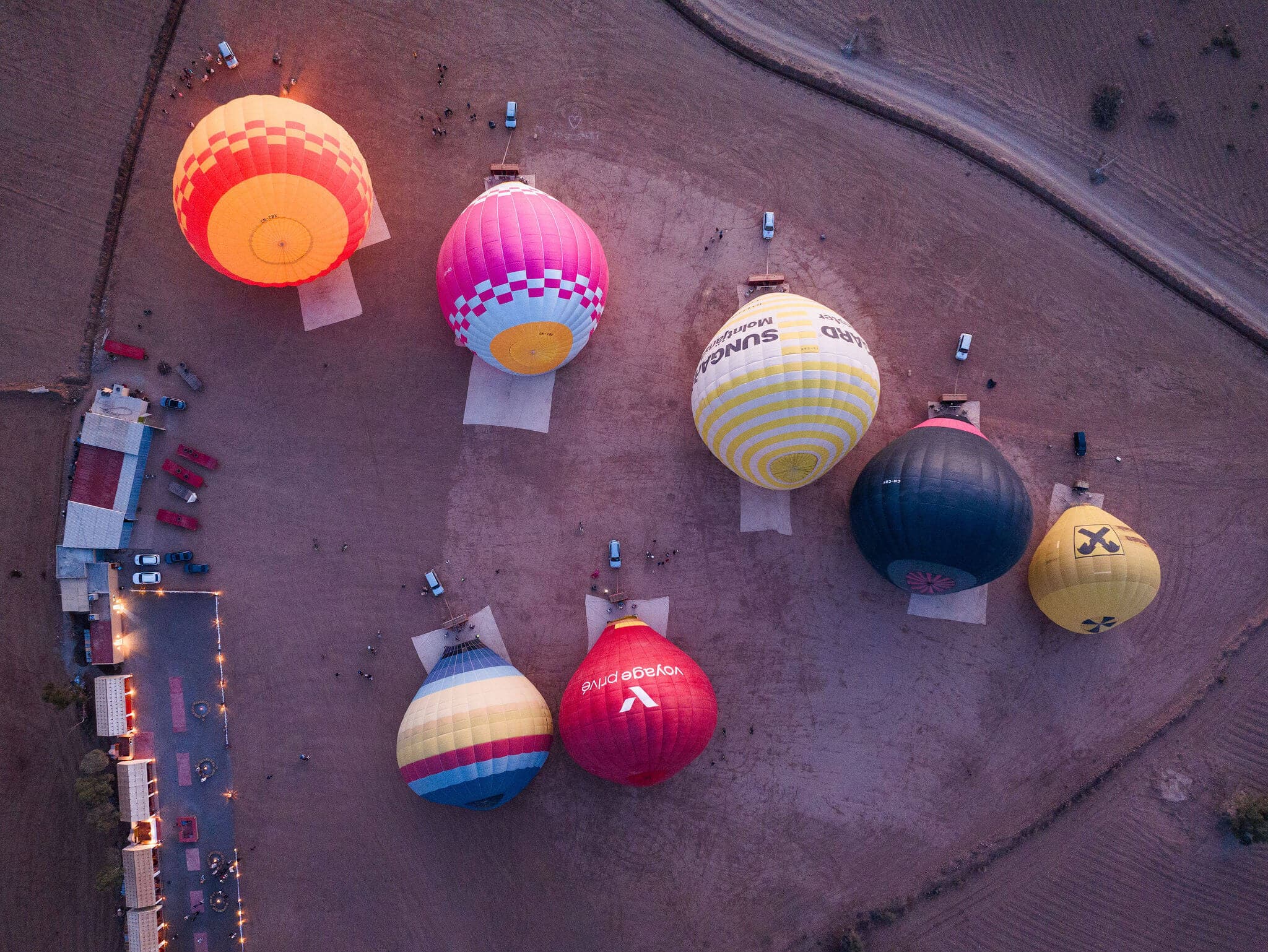 The launch field before dawn, seen from above: balloons being inflated on open ground beside the field buildings